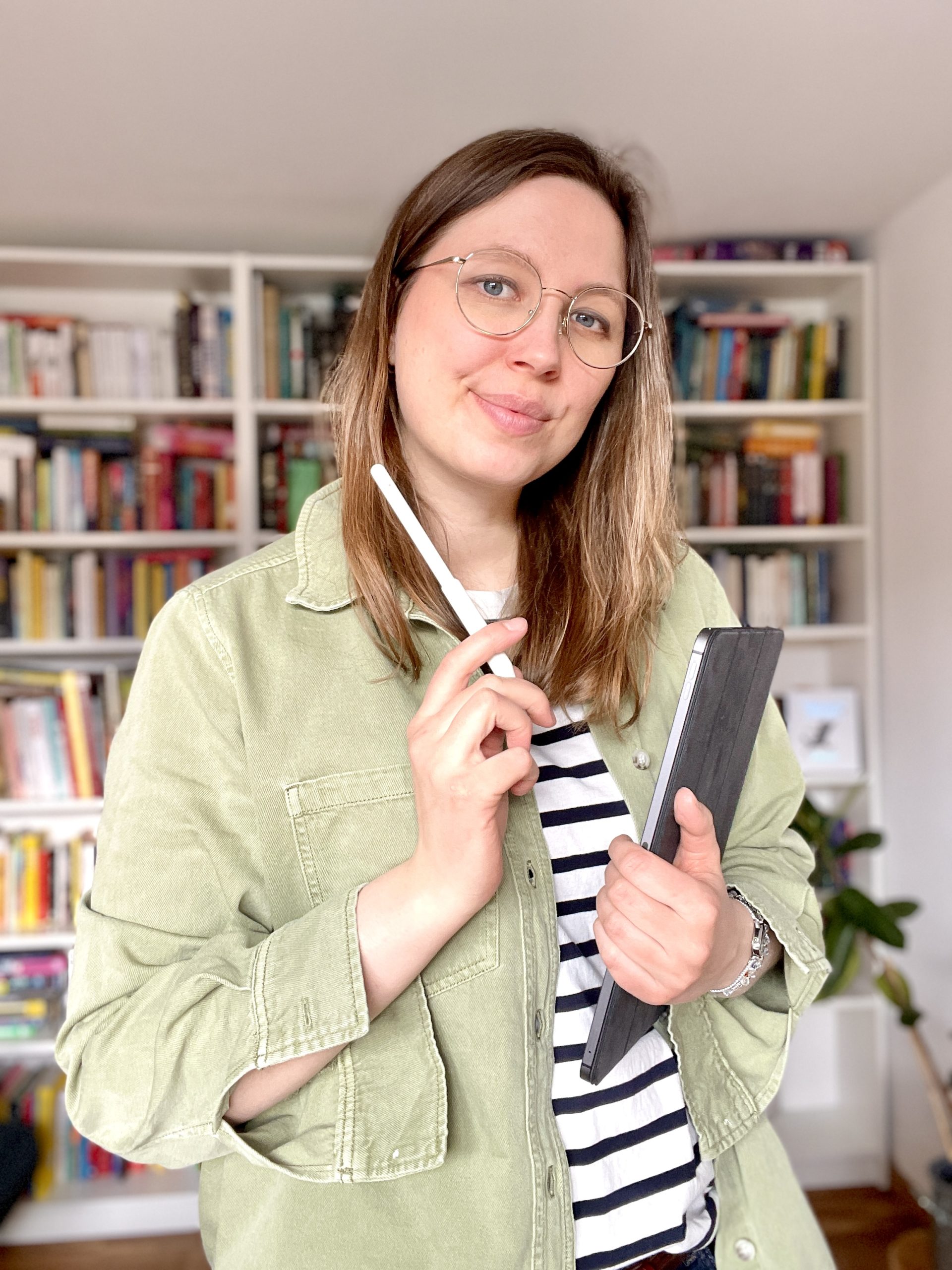 Künstlerin mit ipad und Zeichenstift steht vor einem Bücherregal